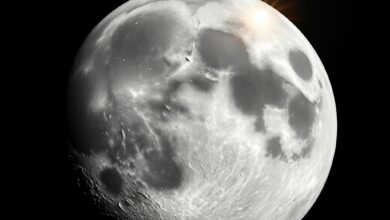 Superfície lunar exibindo cratera de impacto recente com detritos rochosos e solo acinzentado sob luz solar direta